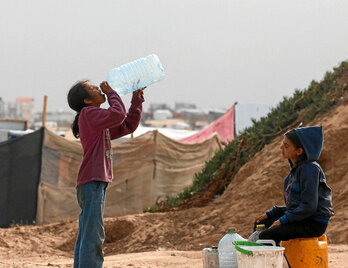 Dos niñas beben agua mientras esperan al camión cisterna en un campo de desplazados en Rafah.